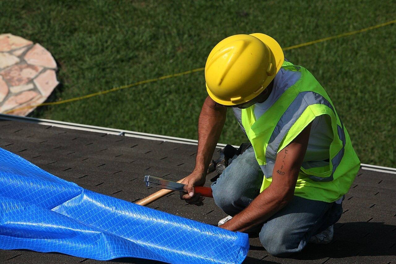 A worker installs a blue tarp on a roof in Texas